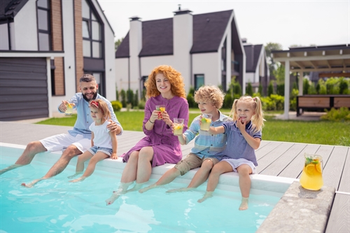 A family sitting on the side of a garden swimming pool dangling their legs in the water