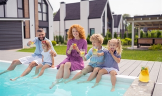 A family sitting on the side of a garden swimming pool dangling their legs in the water A family sitting on the side of a garden swimming pool dangling their legs in the water