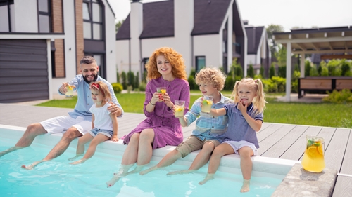 A family sitting on the side of a garden swimming pool dangling their legs in the water A family sitting on the side of a garden swimming pool dangling their legs in the water